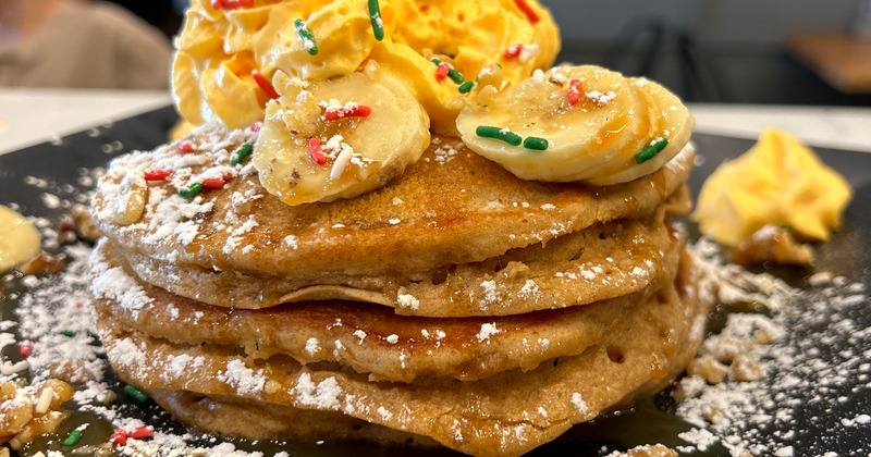 Stack of pancakes topped with banana, whipped cream and sprinckles