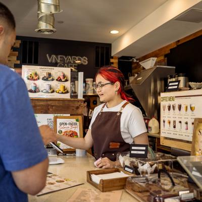 Barista wearing a brown apron while serving a customer behind a counter.