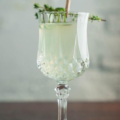 Light cocktail in a cut glass goblet with herb garnish.