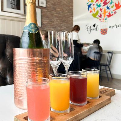 A champagne bottle in a copper ice bucket with two flutes is next a mimosa flight.