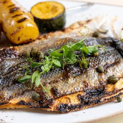 Grilled fish with herbs and capers, served with grilled vegetables and charred lemon.