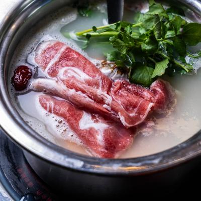 Hot pot dish featuring sliced beef and fresh herbs.