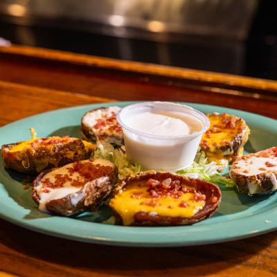 Loaded potato skins served on a green plate with a side of dipping sauce.