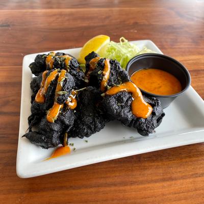 Black chicken karaage served with a dipping sauce and a lemon wedge.