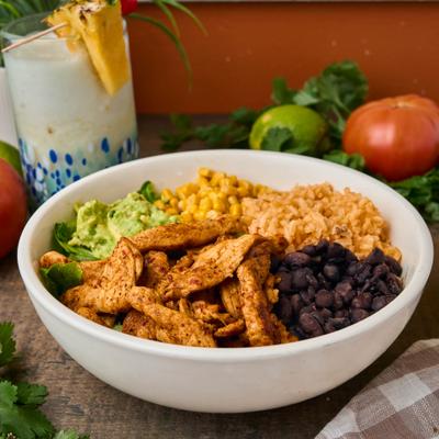 Chicken rice bowl topped with black beans, corn, guacamole, and greens.