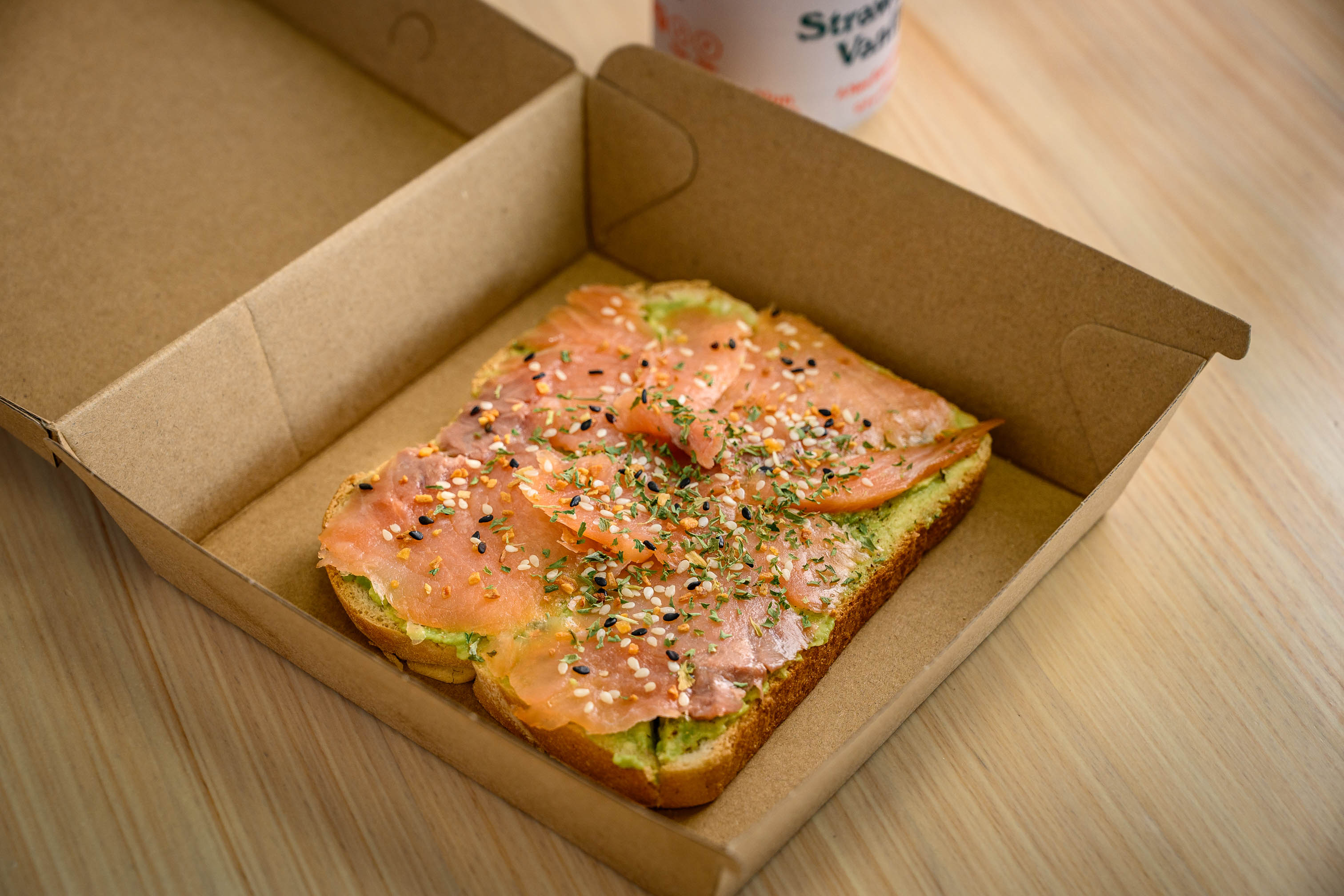 Smoked salmon and avocado toast with seasoning inside a cardboard takeout box