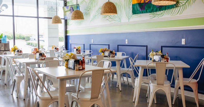 Bright dining area with white tables, large windows, and a palm-leaf mural