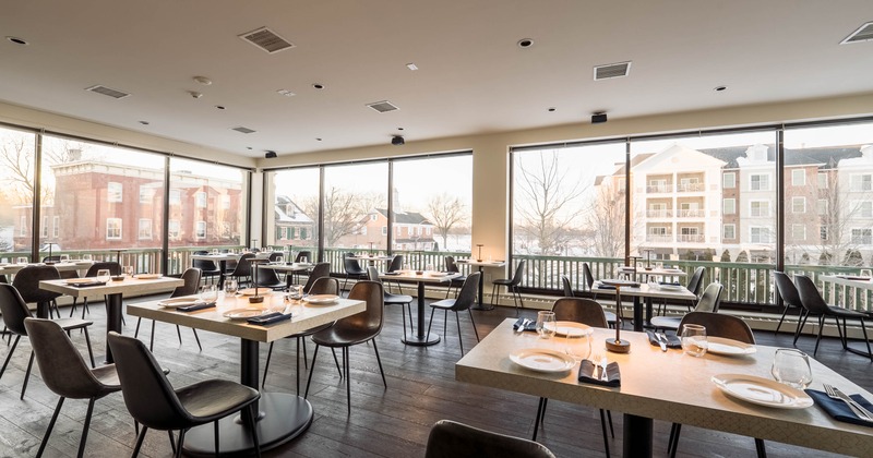 Interior dining area with large windows, set tables, and brown chairs