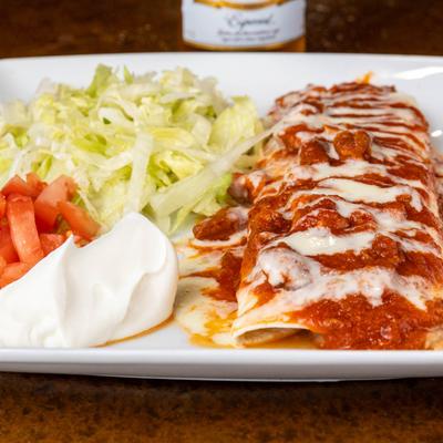 Burrito smothered in cheese and spicy sauces, served with salad, and sour cream.