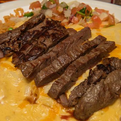 Sliced carne asada steak served over melted cheese and pico de gallo.