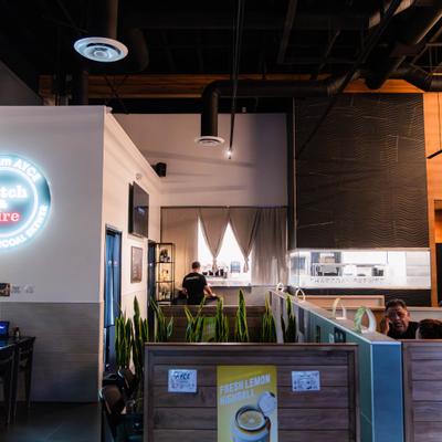 Restaurant interior with a neon circular sign, wooden booths, and open kitchen.