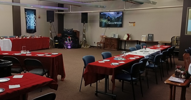 An event room with tables covered in red linens, with white plates and napkins spread around them, surround an event room.