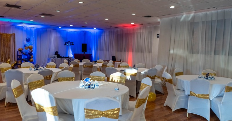 Event space with round tables, white chairs with gold sashes, and decorative lighting