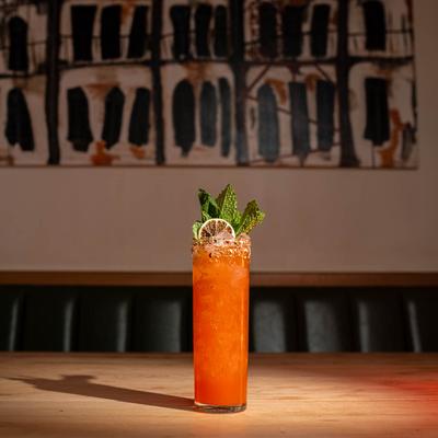 Orange Cool Runnings cocktail sits on a table, in front of abstract mural art.