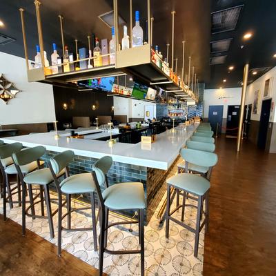 Bar aera featuring an overhead floating liquor rack, a counter and bar stools.