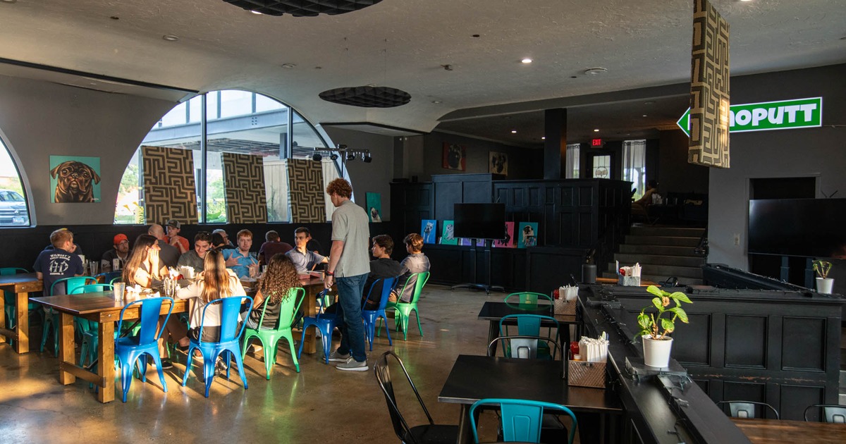 Group of people dine and socialize at tables in a modern restaurant with large windows and artwork