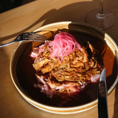 Braised pork shank served over vibrant red slaw with pickled onions on top.