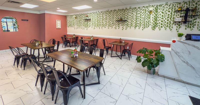 A modern interior - wooden tables, black metal chairs and artificial green vines on the wall