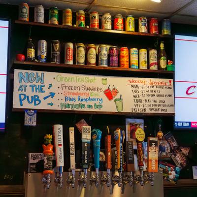 Bar with a variety of beer brands on shelves and tap handles and a handwritten menu.