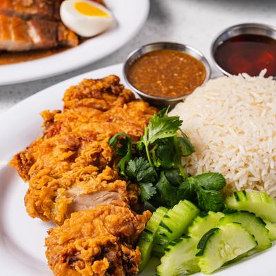 Fried chicken served with rice, cucumber slices, dipping sauces and herbs.
