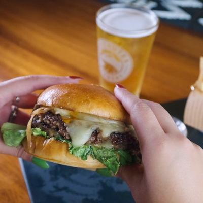 Hands holding a burger with glass of beer in the background.