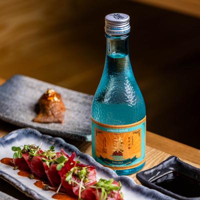 Blue glass sake bottle next to a tuna sashimi plate.