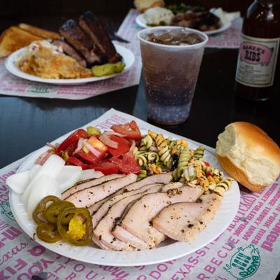 A plate of sliced turkey breast and sides served on a table with other BBQ dish plates.