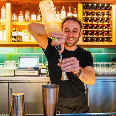 Bartender smiling while pouring spirit into a jigger at Gather in Berkeley restaurant.