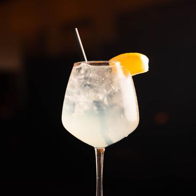A Spritzer in a stemmed glass with ice and a lemon wedge garnish.
