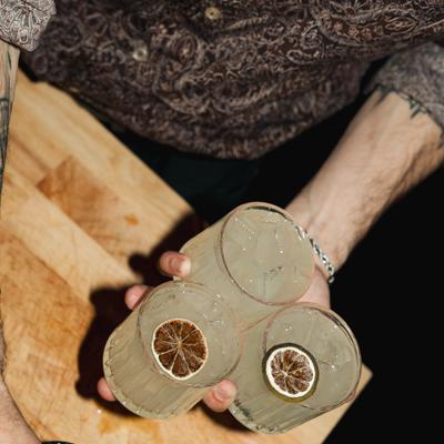 A person holding three glasses of iced drinks garnished with dried citrus slices.