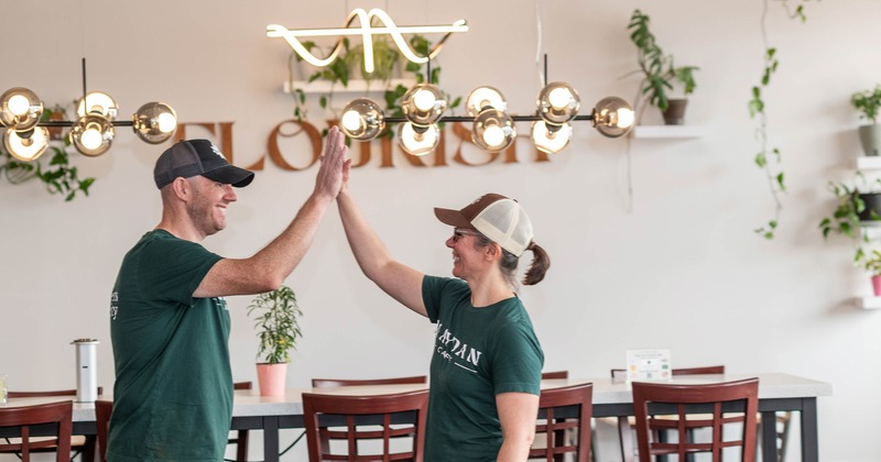 Two individuals sharing a high-five in a cafe with a neon sign