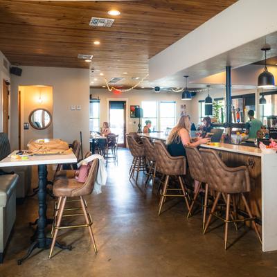 Interior, patrons sit on cushioned bar stools and at tables.