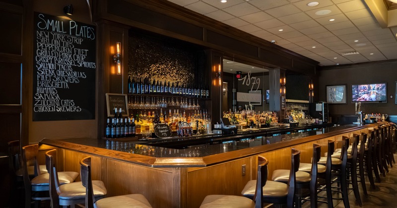 Interior, bar area, long wooden top bar with stools, large stocked liquor shelves in the back