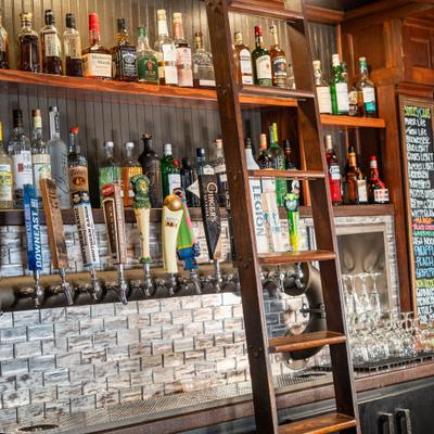 Bar with numerous beer taps, rolling wooden ladder and shelves with various spirits.