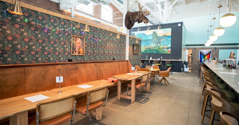 Interior of a restaurant with vintage decor, wooden tables, floral wallpaper, and a bar area