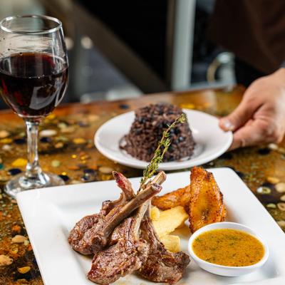 Lamb chops served with a glass of red wine and a side of rice.