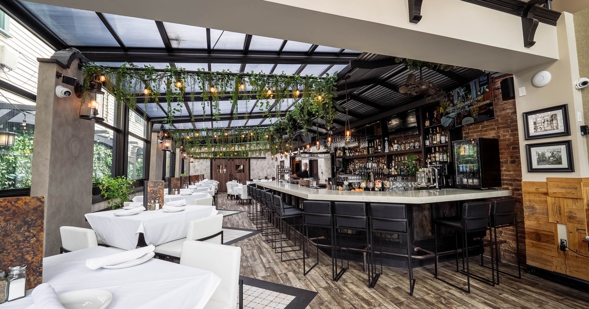 Stylish interior - a long bar, plants, tables with white tablecloths under a conservatory-style roof