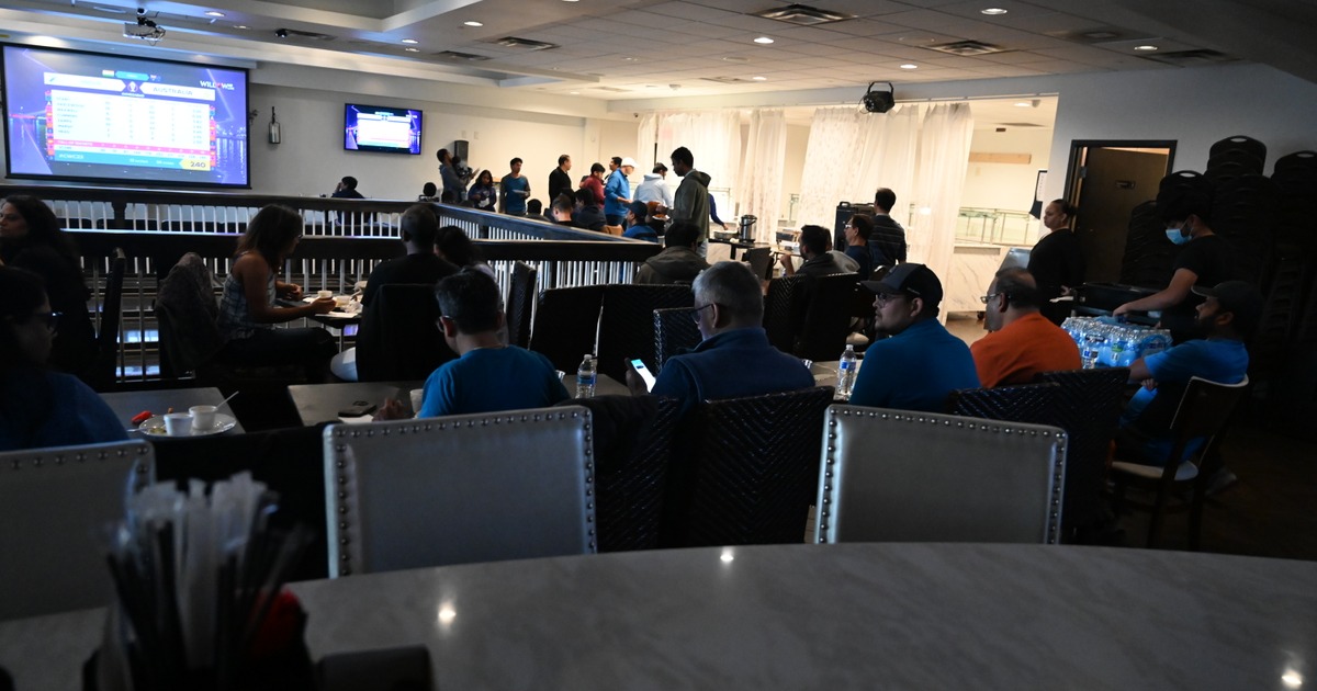 A group of people in a dimly lit room watches large screens showing sports