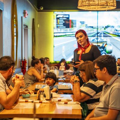 A server stands by a family dining at a restaurant with racing screens.