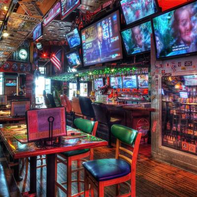 A lively sports bar with multiple TVs, tables with menus, colorful chairs, a well-stocked bar