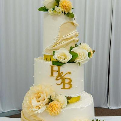 Multi-tier white and gold wedding cake decorated with floral accents and a personalized monogram.
