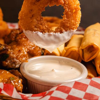 Onion ring being dipped in a sauce on a tray with assorted fried appetizers.