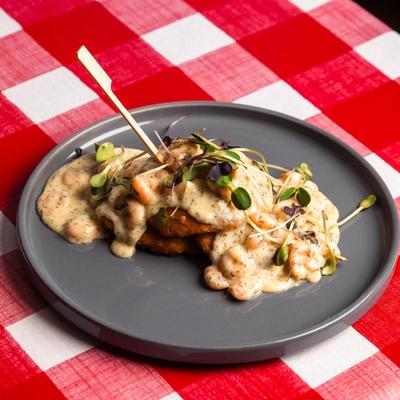 A gray plate holds Crab Cakes topped with creamy sauce on a red checkered table.