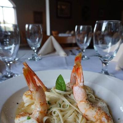 Shrimp linguine garnished with basil on white plate, empty wine glasses in the background.