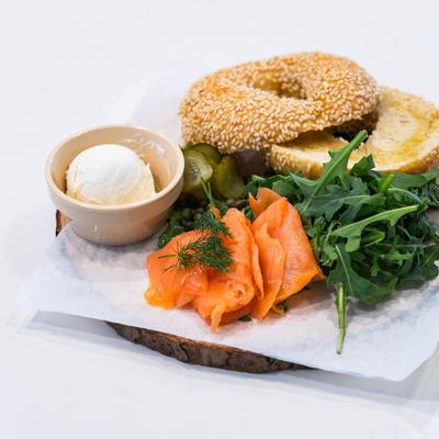 A sesame bagel with cream cheese, arugula, smoked salmon garnished with dill, and pickles.