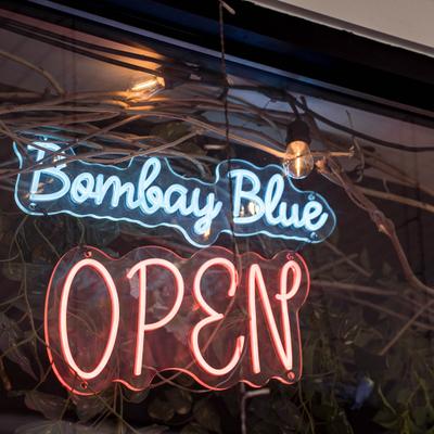Neon sign reading Bombay Blue Open.