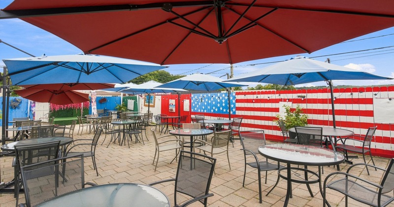 Outdoor patio with metal tables, colorful umbrellas, and American flag mural