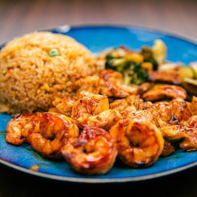 Glazed shrimp with fried rice and vegetables on a blue plate.