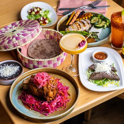 Mexican dinner spread with braised meat, blue corn tortillas, black beans, and cocktails.