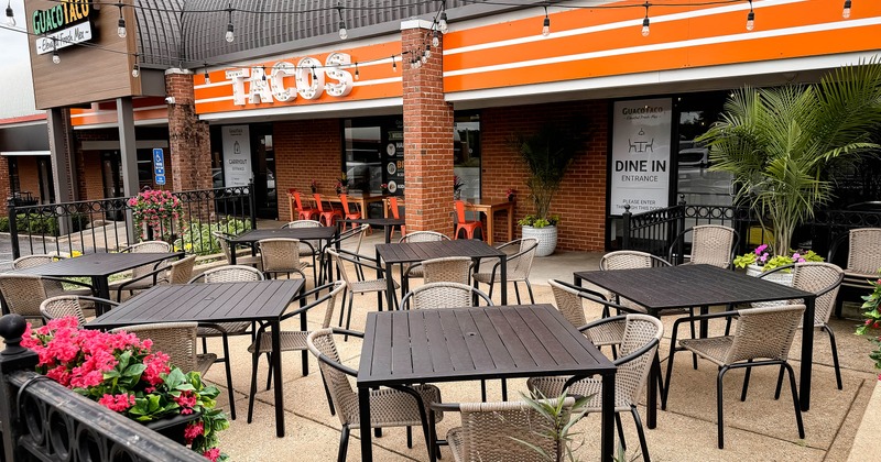 Exterior, restaurant front, seating area encircled by metal railing, tables for four